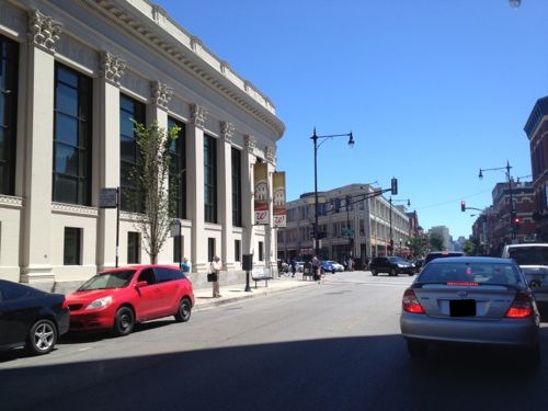 The busy corner has pedestrians, cyclists, and lots of auto traffic. The Walgreens is on the left. 