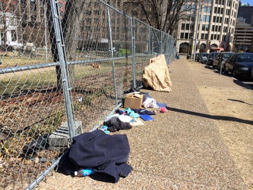 Belongings of the homeless surround the park at the base of the construction fence. 