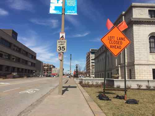 The two signs on the sidewalk were reduced to one on the grass. 